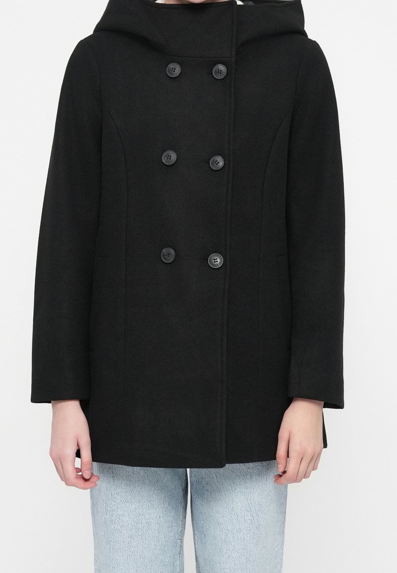 Black double-breasted coat with hood worn over light blue denim jeans, shown from shoulders to hips against a plain background.