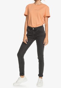 Oranžové bavlněné tričko s krátkými rukávy a kulatým výstřihem, doplněné černými skinny džíny a bílými teniskami.