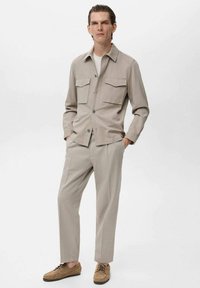 Chemise beige à boutons avec deux poches poitrine, associée à un pantalon assorti. Les chaussures sont en suède marron clair avec des lacets. Design simple et moderne.