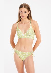 Zelená květinová bikiny souprava s trojúhelníkovým topem, který má tenké ramínka a texturovaný design; spodní díl se zavazuje na bocích a má podobný květinový vzor.