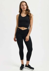 Zwart atletisch crop top met een afgeronde halslijn, gecombineerd met een high-waist legging met een crossover-ontwerp en logo-accent.