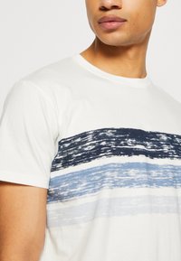 Weißes Baumwoll-T-Shirt mit einem horizontalen Streifenmuster in Marineblau, Blau und Hellblau. Rundhalsausschnitt und kurze Ärmel.