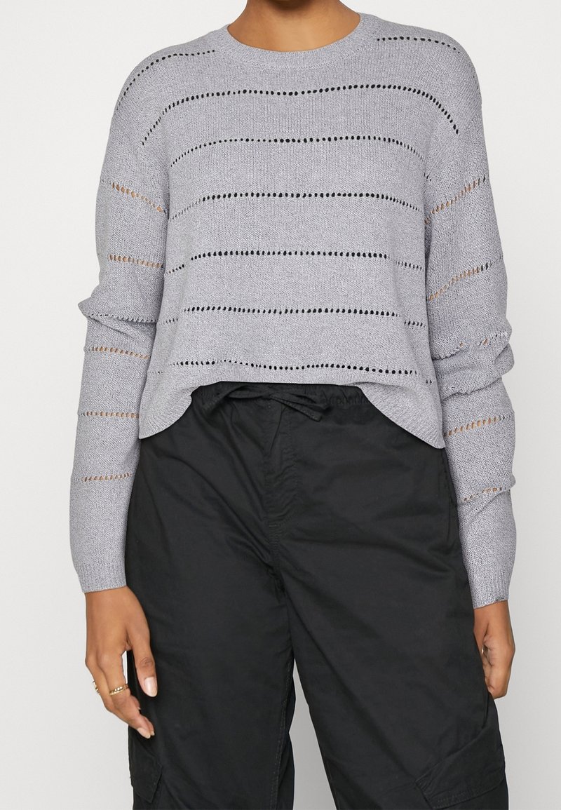 Gray knit sweater with horizontal stripes and openwork detailing, rounded neckline, and gathered sleeve cuffs, paired with black cargo pants.