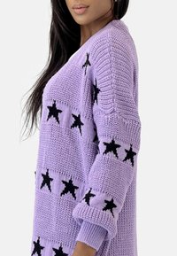 Suéter de punto morado con patrón de estrellas negras, que presenta mangas oversized y una tela texturizada. El diseño tiene un corte relajado y puños acanalados.