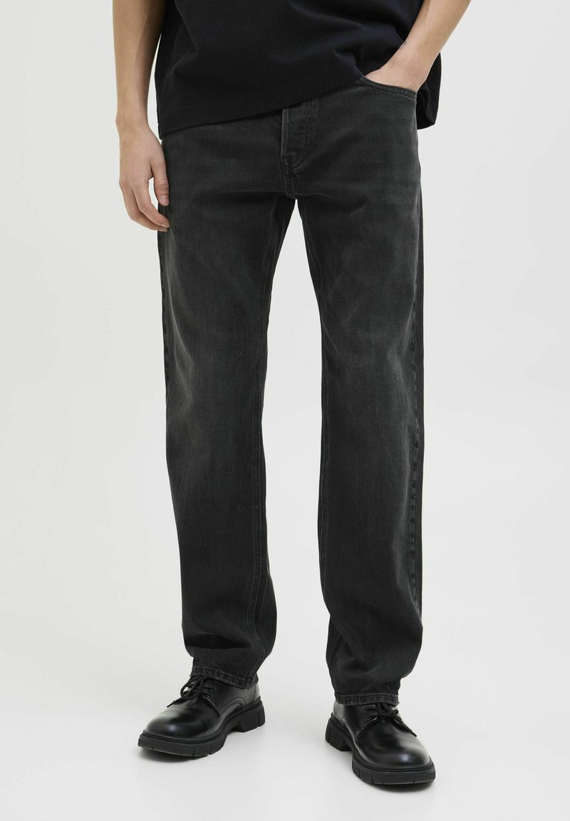 Jeans de mezclilla negra con un diseño de pierna recta, con bolsillos delanteros y un acabado desgastado. Combinados con zapatos negros de cordones.