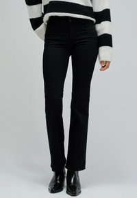 Jeans negros de campana con una cintura alta, combinados con un suéter a rayas. Los jeans tienen una textura suave y un ligero estiramiento.