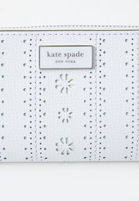 White leather wallet with perforated design, featuring cut-out flower patterns and a silver logo plaque reading "kate spade NEW YORK."