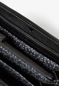 Portafogli in pelle nera con hardware argentato, caratterizzato da più scomparti foderati con un materiale a motivo floreale grigio. Chiusura con zip.