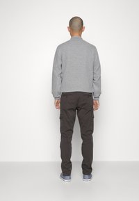 Gray quilted bomber jacket with ribbed cuffs, paired with dark cargo pants featuring side pockets, viewed from the back. Casual sneakers complete the look.