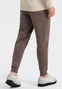 Brune sweatpants med taperet pasform og ribstrikkede manchetter, parret med lyse sko med tekstureret design og sort gummisål.