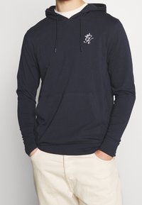 Námořnická bavlněná mikina s přední kapsou, kapucí na šňůrku a vyšívaným logem na hrudi. Dlouhé rukávy s žebrovanými manžetami.