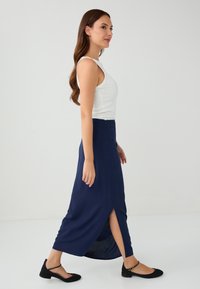 Marineblauer Maxirock mit seitlichem Schlitz, aus leichtem Stoff, kombiniert mit einem weißen Tanktop und schwarzen Ballerinas. Einfaches und figurbetontes Design.