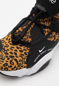 Zapatilla negra y naranja con un diseño de estampado de leopardo, parte superior de tela texturizada, acentos negros y un logo de Nike blanco con texto.