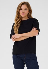 Black cotton t-shirt with a crew neck, short sleeves, and a relaxed fit, paired with dark blue jeans. Smooth texture, minimal design.