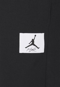 Tela negra con una etiqueta blanca rectangular que presenta un logotipo en silueta negra y el texto "Vuelo" en cursiva debajo.