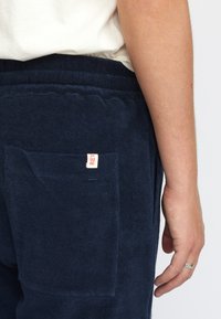 Marineblauwe badstof broek met een achterzak voorzien van een klein rood label met de tekst "REV." Zachte textuur met een elastische tailleband.