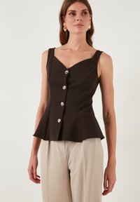 Rjav peplum top z V-izrezom, ki ima pet kovinskih gumbov in široke naramnice, v kombinaciji s bež hlačami. Gladka tekstura tkanine.