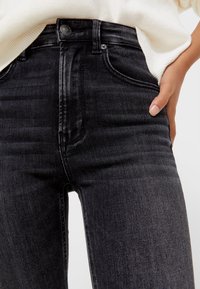 Jeans de mezclilla negro de cintura alta, con un corte ajustado, diseño de cinco bolsillos y detalles de costura sutiles. Textura suave con ligeras decoloraciones.