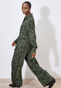 Green and black zebra-striped outfit with a collared top and wide-leg pants, featuring a soft, textured fabric and relaxed fit.