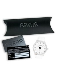 Montre blanche avec un boîtier en acier inoxydable argenté, au design minimaliste, aiguilles noires et bracelet en cuir blanc. Comprend une carte de garantie noire et une boîte.
