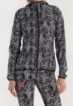 Chaqueta con cremallera y leggings a juego con estampado de piel de serpiente en blanco y negro y una raya diagonal roja en el muslo izquierdo.