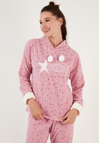 Conjunto de pijama rosa de felpa con capucha, que presenta una estrella blanca y el texto "SHINE". Puños blancos esponjosos y pompones acentúan el diseño.