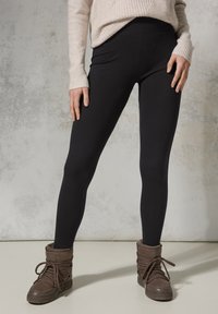 Zwarte leggings met een zachte textuur, gecombineerd met bruine laarzen met een bontvoering, met veters en een lichtjes slouchy ontwerp.