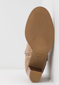Semelle d'une bottine beige en daim avec talon bloc, montrant les motifs de la semelle et le nom de la marque "San Marina" avec la taille 37.