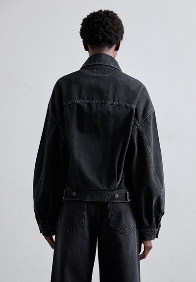 Black denim jacket featuring a loose fit, dropped shoulders, and snap button accents on the waistband and cuffs.