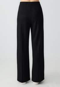 Pantalons noirs à jambes larges en tissu lisse. Dotés d'une taille ajustée et de coutures arrière discrètes pour la structure. Pas de poches visibles.