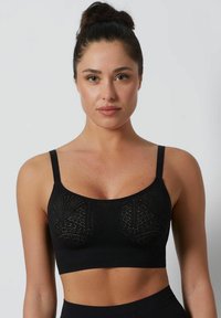 Sujetador inalámbrico negro con tirantes anchos, que presenta un patrón texturizado y un diseño sin costuras. Banda elástica en la parte inferior para mayor soporte.