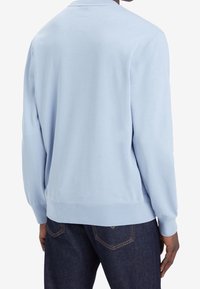 Sudadera azul claro con cuello redondo, mangas largas y puños acanalados, combinada con jeans de mezclilla oscura. Diseño simple, textura de tela suave.