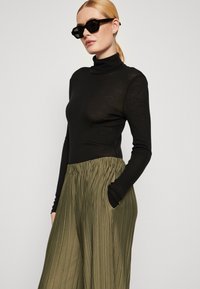 Melnā ribota turtlenecka blūze ar garām piedurknēm, apvienota ar olivu zaļām, nožņaugšanas platām biksēm, kurām ir sānu kabatas. Gludās melnās saulesbrilles.