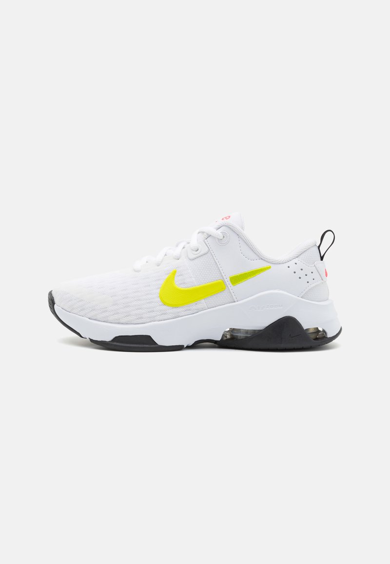 Zapatilla deportiva blanca con parte superior de malla, swoosh en amarillo neón, detalles en negro y suela blanca, que presenta un sistema de amortiguación de aire visible.