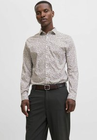 Camicia a maniche lunghe con colletto, caratterizzata da uno sfondo beige chiaro con un motivo floreale marrone. Realizzata in tessuto morbido, design aderente, abbinata a pantaloni scuri.
