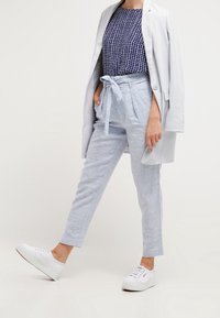 Ljusgrå linnebyxor med knytbar midja, kombinerat med en topp i marinblått rutmönster och en ljusgrå kavaj. Vita sneakers fulländar outfiten.