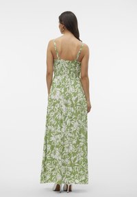 Zelené květinové maxi šaty s bílými vzory. Mají smockovaný zadní díl, tenké ramínka a vzdušný siluetu. Hladká látka s lehkým texturovaným povrchem.