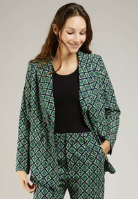 Blazer à motifs verts et bleus avec un design géométrique, doté de larges revers et d'un fit décontracté. Associé à un haut noir.