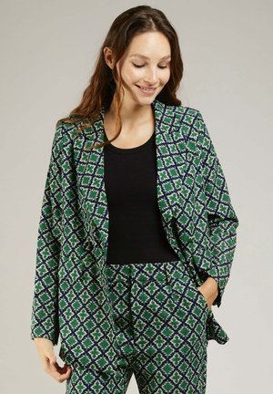 Blazer à motifs verts et bleus avec un design géométrique, doté de larges revers et d'un fit décontracté. Associé à un haut noir.