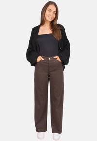 Cardigan noir en maille porté sur un haut noir ajusté, associé à un pantalon large marron taille haute et des baskets blanches.