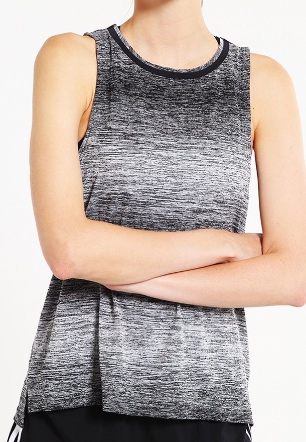 Personne portant un haut de sport sans manches en dégradé gris et noir, bras croisés sur un fond blanc uni.