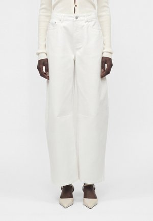 Μοντέλο που φοράει λευκό παντελόνι με ψηλή μέση και φαρδιά πόδια με εμπρόσθιες τσέπες, σε συνδυασμό με κρεμ ribπλό ζακέτα με κουμπιά και μπεζ μυτερές γόβες.