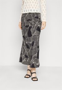 Gonna maxi nera con motivi ondulati bianchi; tessuto morbido che si adagia dolcemente. Abbinata a sandali neri con strap.