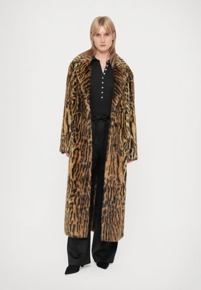 Casaco de pelagem falsa com padrão de leopardo, de design longo e fluido, gola larga e botões pretos. Usado sobre uma blusa e calças pretas.