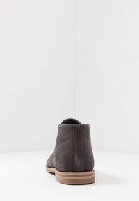 Bottine en daim gris au design épuré, bout arrondi et semelle en caoutchouc couleur noisette. Détails de coutures le long des côtés.