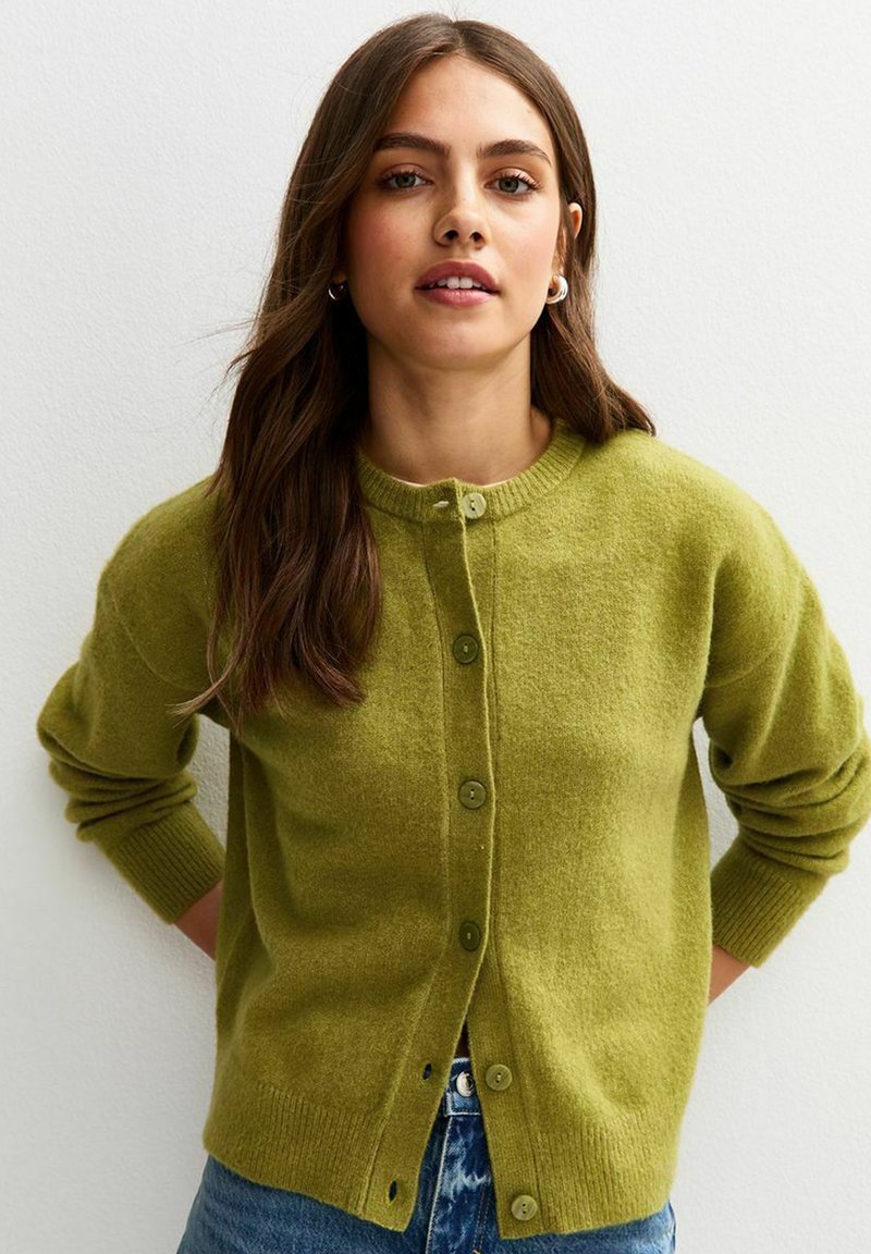 Groene cardigan van zacht materiaal, met een ronde halslijn, een knoopsluiting aan de voorkant en geribde manchetten. De textuur lijkt gezellig en warm.