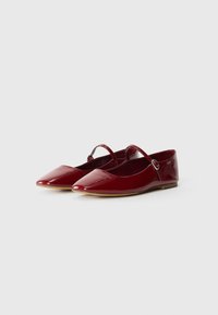 Ballerines en cuir laqué rouge avec un bout pointu, une bride au niveau de la cheville et une finition lisse et brillante. Semelle discrète.