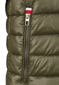 Grüne Steppweste mit gequilteten Abschnitten, ausgestattet mit einem metallischen Reißverschluss, roten, weißen und blauen Stoffakzenten oben und glatter Textur.