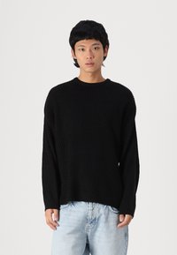 Suéter negro de punto con diseño de relieve, cuello redondo y corte holgado, combinado con jeans de mezclilla azul claro.