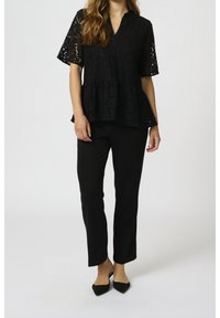 Top peplum in pizzo nero con maniche corte e scollo a V; abbinato a pantaloni neri aderenti e tacchi a punta. Tessuto e design eleganti.